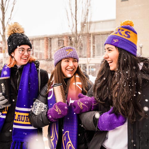 three students sitting outside on waterloo campus in the fall