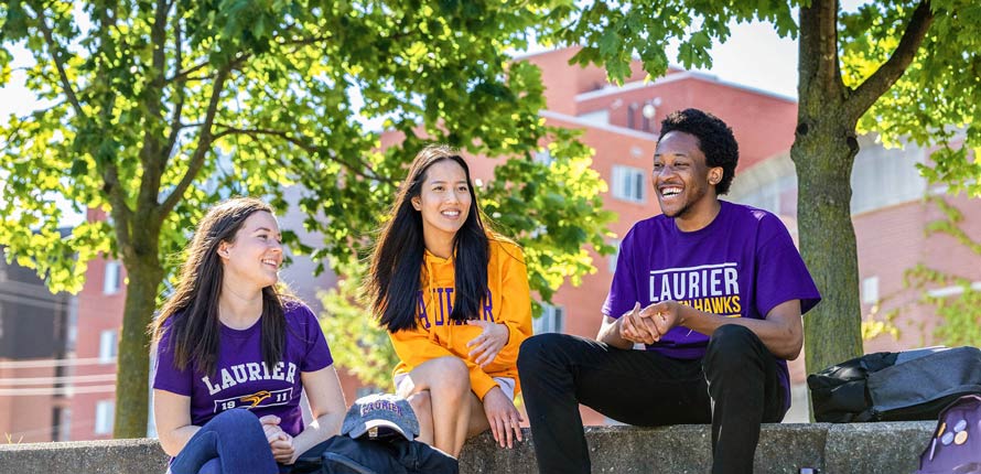 three students sitting outside on waterloo campus in the summer