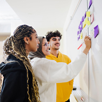 three students writing on white board